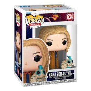 In-box product image of the Funko Pop! Heroes Kara Zor-El with Cedric #634 vinyl figure. The white packaging box displays a cosmic deep space nebula trim and the DC Supergirl logo. Inside the transparent viewing window stands a chibi-style figure of Supergirl with long blonde hair, large black eyes, a blue shirt, and a long brown trench coat. Next to her feet is a small, cream-colored alien caterpillar figure named Cedric with turquoise horns and large blue eyes.